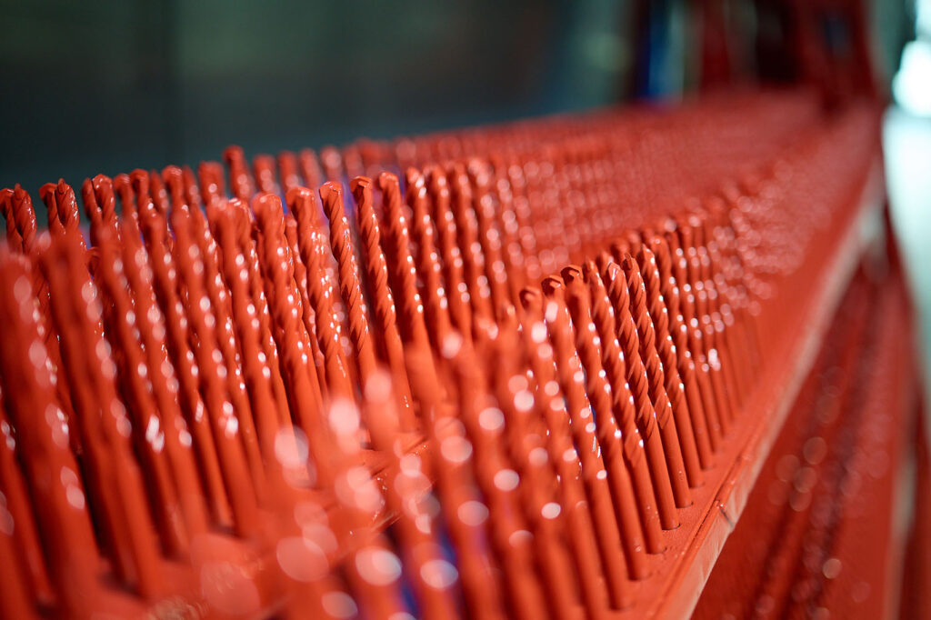 Reihen von mit leuchtend roter Farbe beschichteten Bohrern sind parallel aneinandergereiht, wobei der Fokus auf dem Vordergrund und einem unscharfen Hintergrund liegt. LAC Berger Industrielackierung